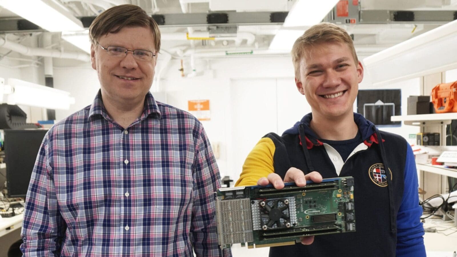 professor and grad student stand in a lab while the student holds out a computer component